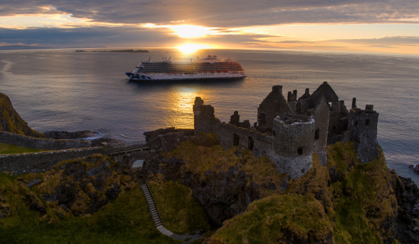 Cruise ship sailing past historic castle ruins near Belfast at sunset
