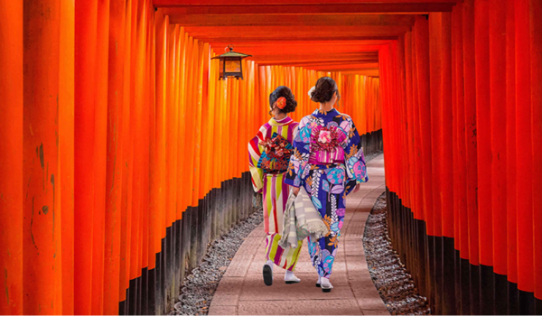 Two people in traditional kimonos walking through a red torii gate pathway in Japan