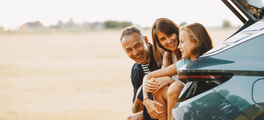 Family of 3 sitting in car boot smiling and going to travel